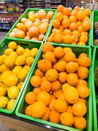 Vibrant green baskets are filled with fresh oranges and lemons, showing a lively array of colors in a grocery store. Shoppers are drawn to the fruit's freshness and appeal.の写真素材