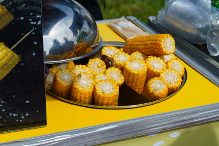 Golden corn cobs arranged neatly on a bright yellow cart, waiting to be enjoyed. The bustling atmosphere of a lively market adds a joyful touch to the scene.の写真素材