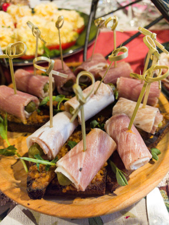 A wooden platter displays an assortment of rolled meats, garnished with herbs and served on a slice of bread. The vibrant colors of nearby dishes create a joyful atmosphere.の写真素材