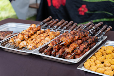 Delicious skewers of marinated chicken and meat sizzle on metal skewers, ready to be enjoyed at a lively summer barbecue. Savory flavors fill the air, enticing all attendees.の写真素材