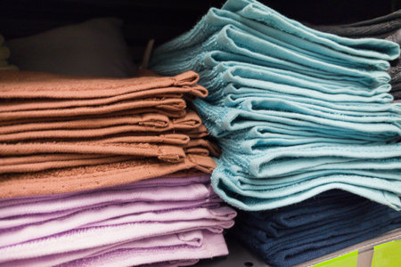 Soft towels in hues of brown, blue, and purple are organized neatly on shelves, showing a variety of fabrics ready for home use, enhancing any bathroom decor with vibrant colors.の写真素材