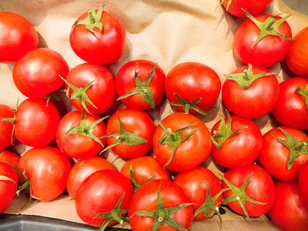 Fresh, ripe tomatoes create a colorful display on brown paper. Glowing in the sunlight, these vegetables showcase their rich color and natural sheen, inviting anyone to savor their flavor.の写真素材