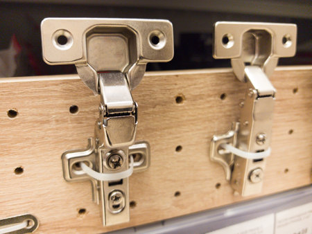 Shiny metal cabinet hinges are mounted on a wooden board, showing their design. The hardware store setting is bright and organized, perfect for DIY enthusiasts and professionals alike.の写真素材