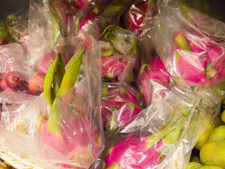 Bright pink dragon fruits are carefully wrapped in plastic, showing their unique shape and colors. This display at a bustling local market invites curious shoppers to explore exotic fruits.の写真素材