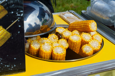 Golden corn cobs arranged neatly on a bright yellow cart, waiting to be enjoyed. The bustling atmosphere of a lively market adds a joyful touch to the scene.の写真素材