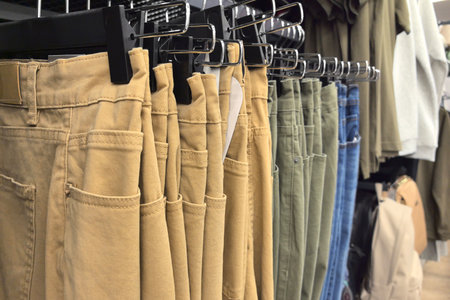 A vibrant display of various pants in shades of khaki, green, and denim hangs on racks. The inviting layout showcases the latest styles in casual clothing at a bustling retail venue.の写真素材