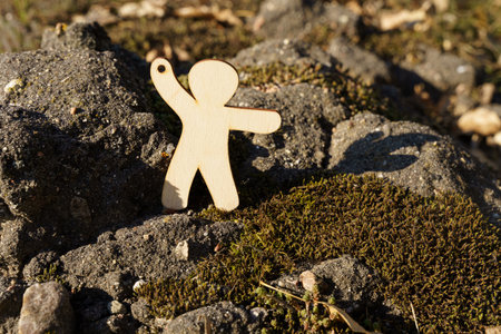 A carved wooden figure stands on moss-covered rocks, extending one arm outward. The natural setting offers a serene backdrop during daylight hours.の写真素材