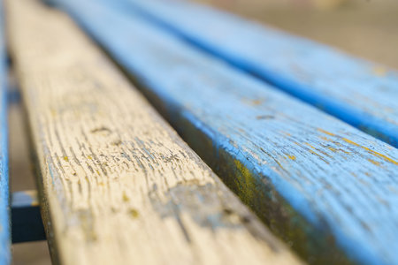 Sunlight illuminates a weathered wooden bench in a peaceful park setting. The aged blue and white paint reveals layers of history while inviting contemplation and relaxation.の写真素材