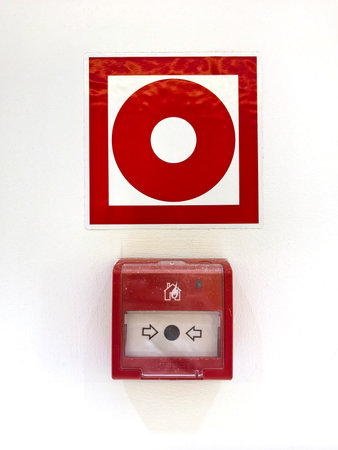 Bold red alert sign paired with a fire alarm switch mounted on a pristine white wall, emphasizing safety measures in public buildings. Clear symbols guide immediate action during emergencies.の写真素材