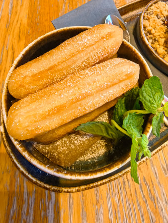 Freshly made churros are presented in a rustic bowl, dusted with sugar and accompanied by a sprig of...