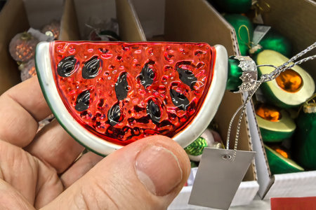 A colorful, handcrafted glass ornament resembling a watermelon slice is held up in a cheerful shop.の写真素材