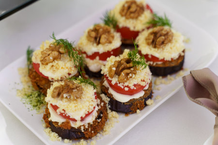 Colorful layers of eggplant and tomatoes rest atop a crunchy base, garnished with walnuts and fresh herbs. This vibrant dish showcases an elegant culinary creation perfect for any gathering.の写真素材