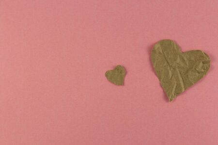 crumpled paper in the shape of two hearts, small and large, on a pink background from natural paper. Copyspace for text.の写真素材