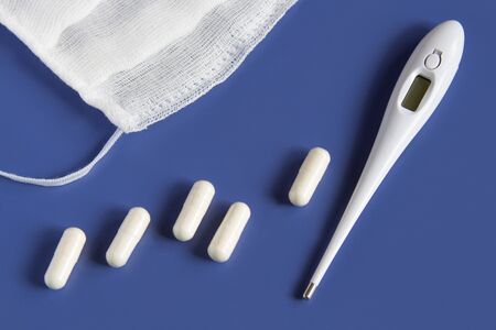 medical mask, white pills and a medical thermometer. On a blue background