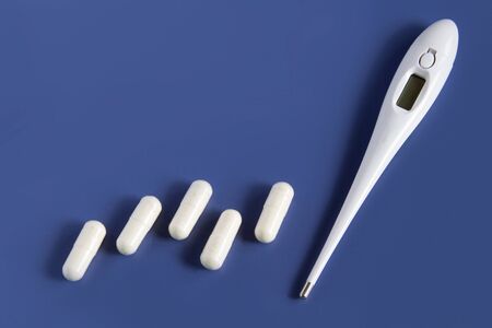 White pills and medical thermometer. On a blue background