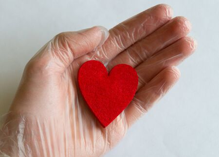 A hand in a transparent glove holds a passionate heart isolated on a background, surgeons save...