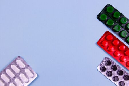 White green black and red pills in blister packs on a blue background photo from the top point....