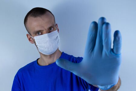 Doctor in a protective mask on a blue background. Holds an outstretched hand in front of him in a...