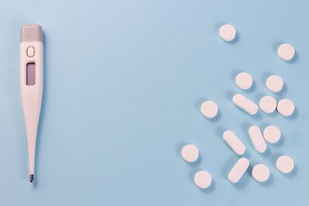 White pills and medical thermometer. On a blue background.