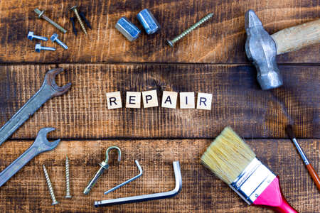 The word repair on wooden background. Nearby different working tools brush hammer wrench screwdriver