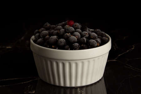 Frozen blueberries and red currants in a white cup on a dark marble backgroundの写真素材