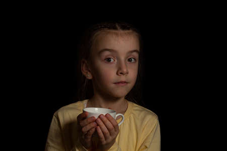 Beautiful portrait of a girl on a dark background. child holding a cupの写真素材