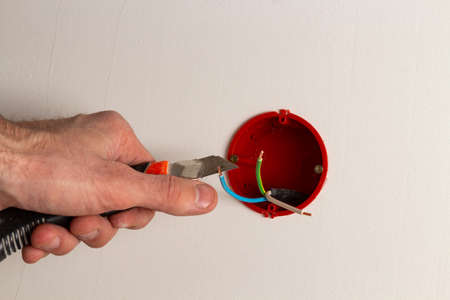 A hand with a knife removes the insulation of wires in a junction box