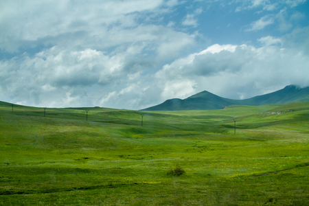 Green Hills and Meadiows, White Clouds and Mountains on the Horizon View through Vehicle Windowの写真素材