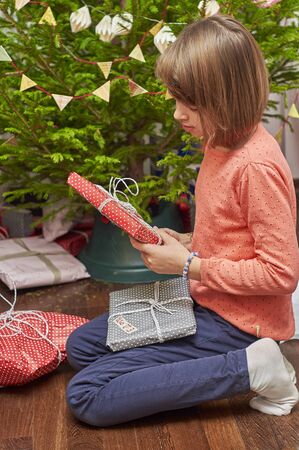 Teenage girl unwrapping Christmas gifts near Christmas tree sitting on the floorの写真素材