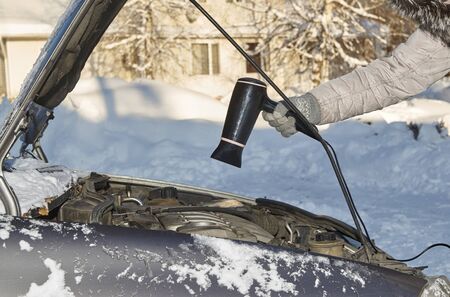  Car owner warming up a motor using hairdryer in cold winter outdoors                               