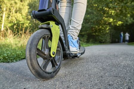 Girl riding on the kick scooter in the park in summer evening close up. Low angle view.