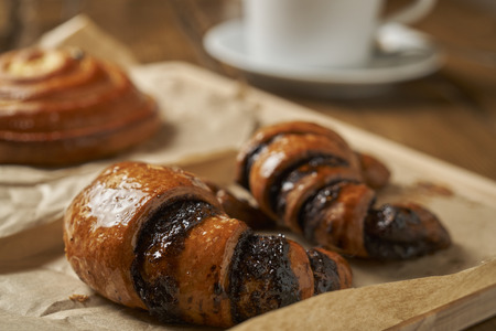 Tasty croissants on the foreground and a cup of tea with a fresh bun on the blurred backgroundの写真素材