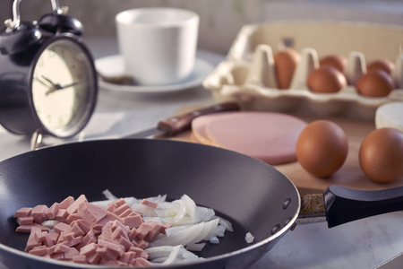 Hasty preparation of a breakfast of fried eggs with sausage and onions in the morning before leaving for workの写真素材