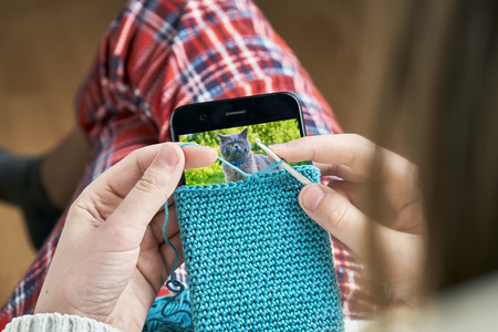 Teen girl's hands knitting a woolen case for a smartphone.の写真素材
