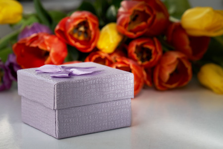 Gift box on the foreground and a bouquet of fresh tulips lying on the table on the blurred background. Gift for a Valentine's day, birthday,wedding,woman's day,mother's day.の写真素材