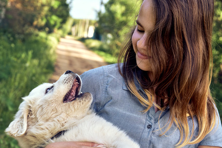 Happy teen girl playing with a cute puppy of a pyrenean mountain dog holding it on her hands in...