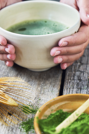 Girls hands holding matcha tea in special matcha tea bowl with bamboo spoon and whiskの写真素材