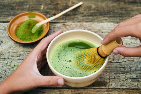 Matcha tea preparation using traditional bamboo whisk on wooden tableの写真素材