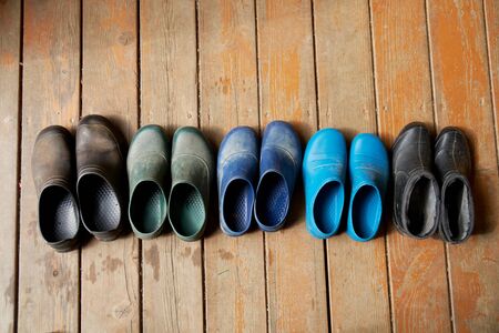 Five pairs of old family rubber boots stand on the wooden floor. Short rubber country goloshes
