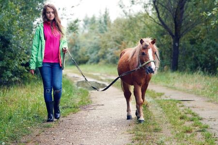 Teenage girl walking with a pony colt on a leash along a country dirt roadの写真素材