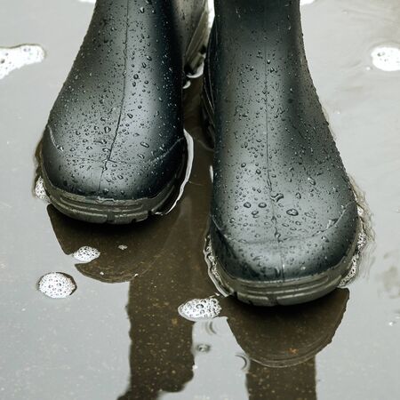 Black rubber boots standing in a puddle on an asphalt road
