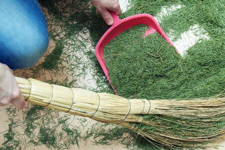 Woman sweeping the floor from dry fallen Christmas tree needles after New Year holidays manually using a broom and a scoop. View from aboveの写真素材