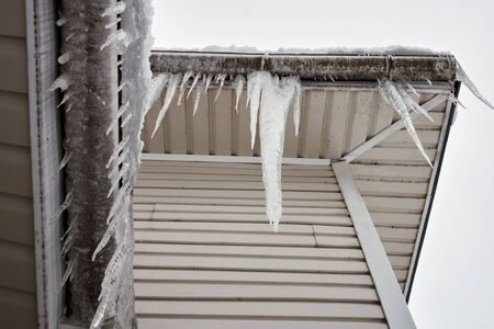 Long heavy icicles hanging on the roof of a house in cold winter