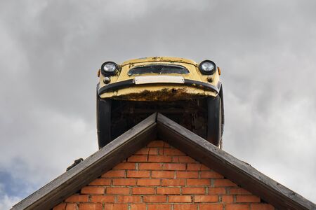Vintage rusty yellow soviet car on a roof of a garage on the cloudy sky background. Bottom viewの写真素材