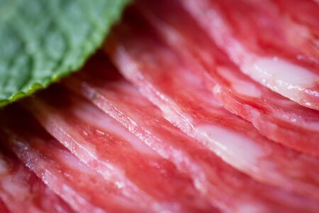 Macro photo of slices of a smoked salami sausage lying like a ladder with a green mint leafの写真素材