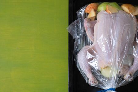 Raw chicken with apples in the plastic oven bag lying on the black baking tray on the green...