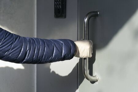 Hand wearing a protective glove opens the door to prevent coronavirus infection.