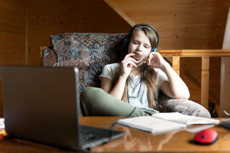 Teen schoolgirl snacks during break in school online webinar. The girl is sitting with her feet on...