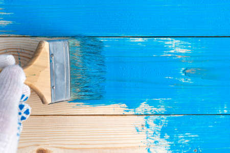 Hand wearing a protective glove paints wooden boards in blue paint with a paintbrushの写真素材
