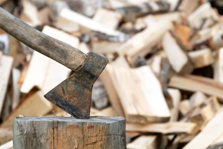 Old rusty axe stuck in a log with a pile of chopped firewood on the backgroundの写真素材